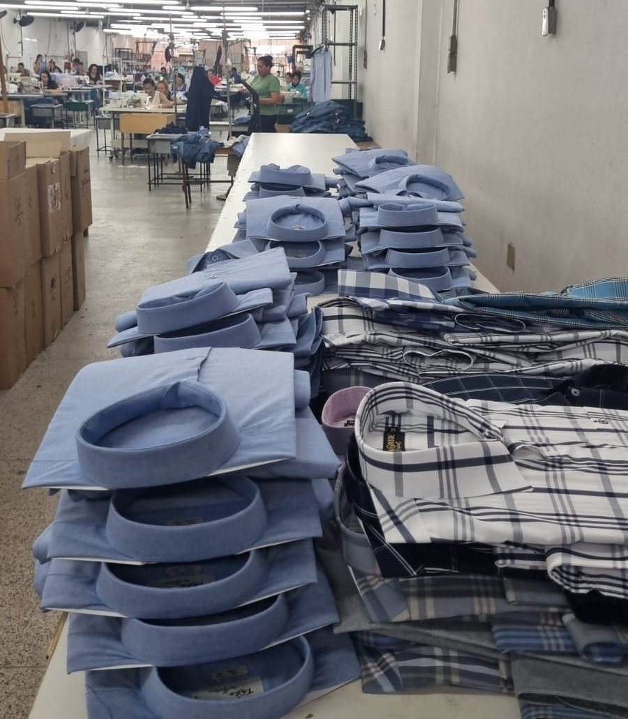 Camisas dobradas e empilhadas em mesas no galpão de produção